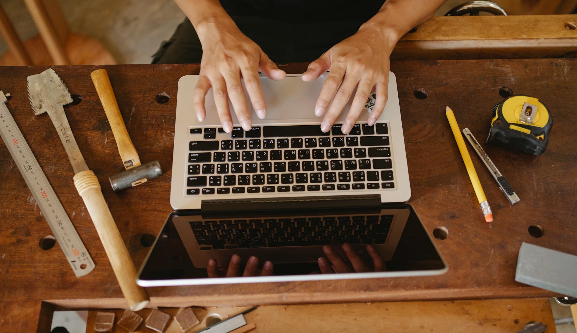Stolarz przy drewnianym stole korzysta z laptopa i narzędzi w warsztacie